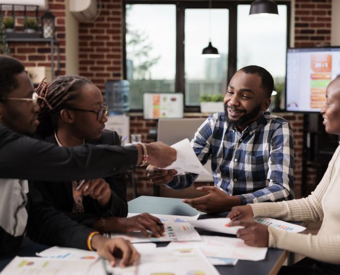 Team of colleagues analyzing business documents in startup office, meeting to do teamwork collaboration on corporate presentation. Working with papers and data information to plan company report.